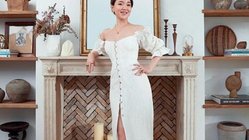 Vivienne Shen, wearing her own Cult Gaia dress, vintage earrings, Bvlgari necklace, vintage rings and Nicholas Kirkwood heels, in front of her 18th‑century‑inspired faux fireplace.